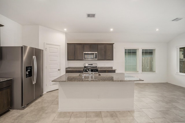 kitchen with a center island with sink, sink, appliances with stainless steel finishes, dark brown cabinets, and light stone counters