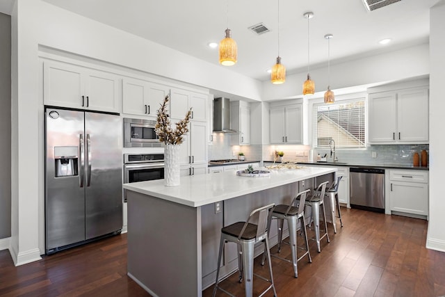 kitchen featuring dark hardwood / wood-style flooring, wall chimney exhaust hood, stainless steel appliances, and decorative light fixtures