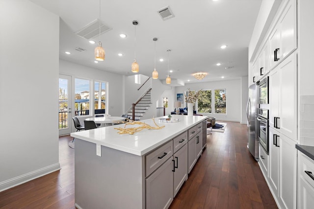 kitchen featuring appliances with stainless steel finishes, white cabinetry, dark hardwood / wood-style floors, a kitchen island, and hanging light fixtures