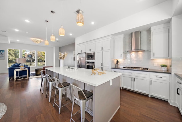 kitchen featuring stainless steel appliances, wall chimney range hood, dark hardwood / wood-style floors, pendant lighting, and a kitchen island