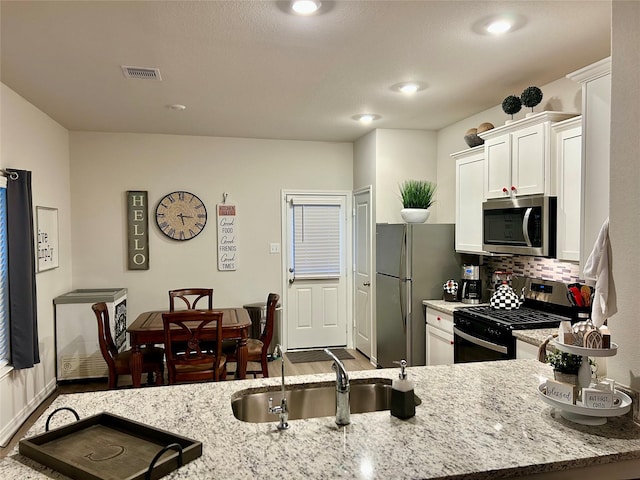 kitchen with appliances with stainless steel finishes, white cabinetry, sink, decorative backsplash, and light stone countertops