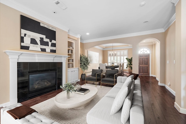 living room with ornamental molding, built in features, a chandelier, a fireplace, and dark hardwood / wood-style floors