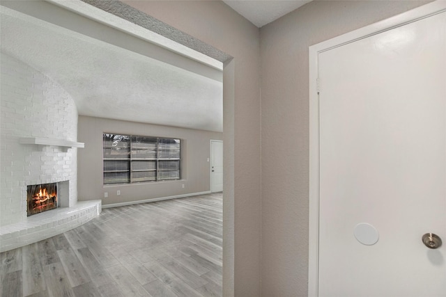 unfurnished living room with a fireplace, a textured ceiling, and light wood-type flooring