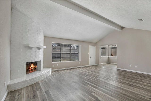 unfurnished living room with a brick fireplace, vaulted ceiling with beams, a textured ceiling, and hardwood / wood-style flooring