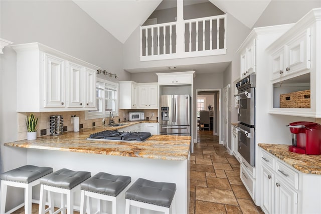 kitchen featuring high vaulted ceiling, white cabinetry, kitchen peninsula, and appliances with stainless steel finishes