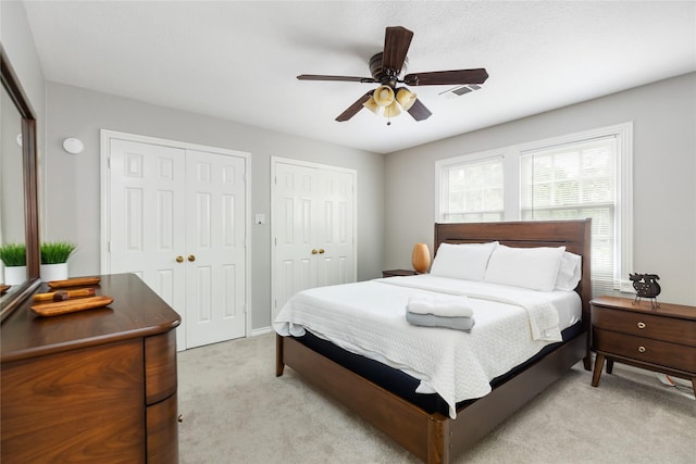 carpeted bedroom featuring ceiling fan and two closets