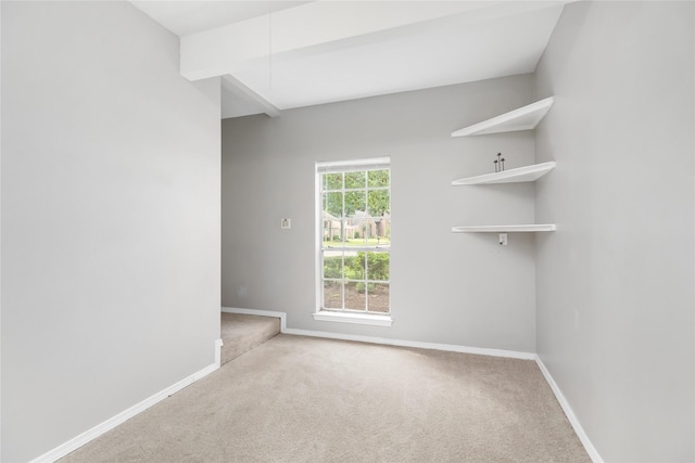 empty room featuring beamed ceiling and light colored carpet