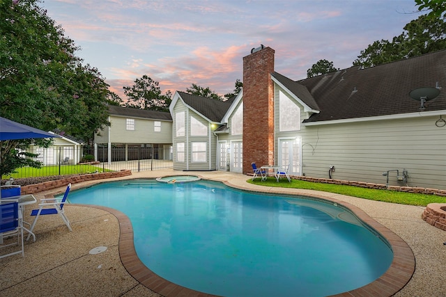 pool at dusk with a patio area and an in ground hot tub