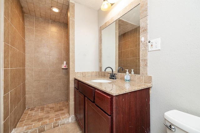 bathroom with tile patterned flooring, vanity, toilet, and tiled shower