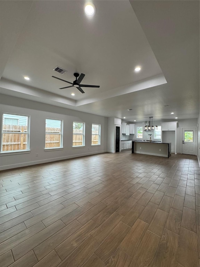 unfurnished living room featuring hardwood / wood-style flooring, a raised ceiling, and ceiling fan