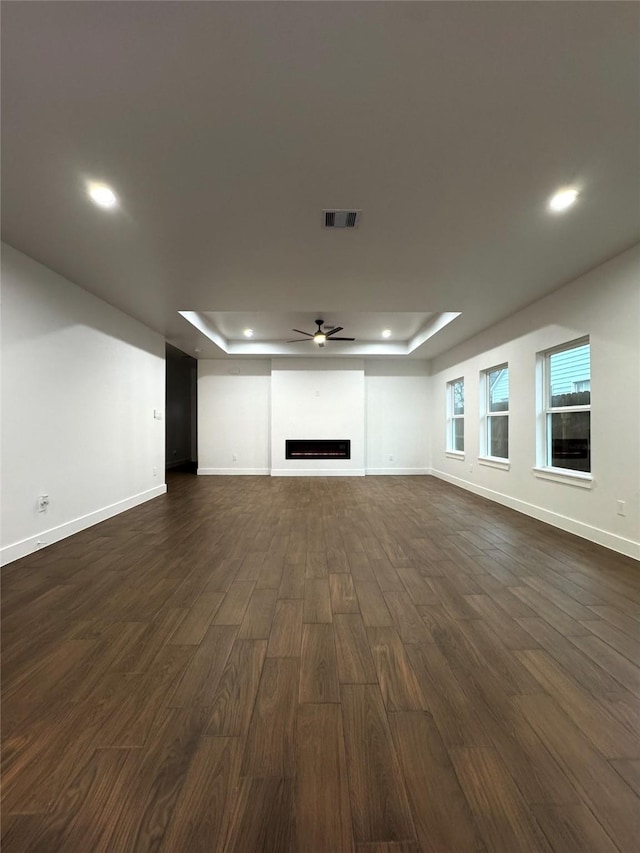 unfurnished living room with ceiling fan, dark hardwood / wood-style flooring, and a raised ceiling