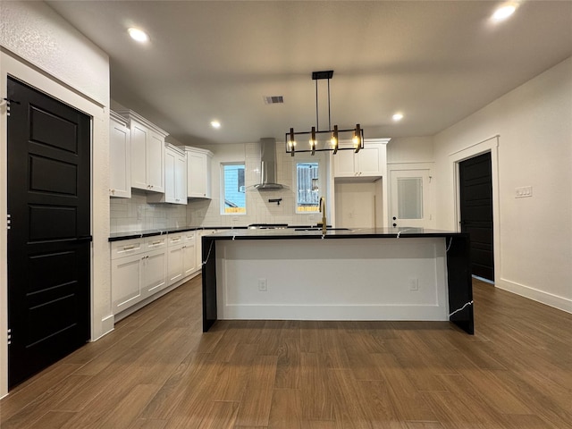 kitchen with white cabinetry, a center island with sink, and wall chimney exhaust hood