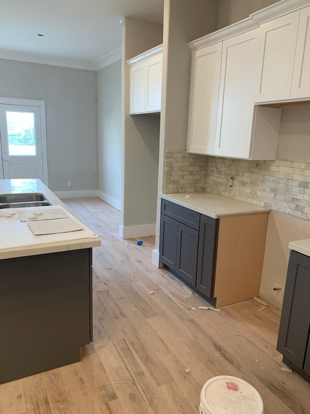 kitchen featuring decorative backsplash, light hardwood / wood-style floors, white cabinetry, and ornamental molding