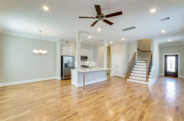 kitchen with white cabinets, a center island with sink, light hardwood / wood-style flooring, ornamental molding, and appliances with stainless steel finishes