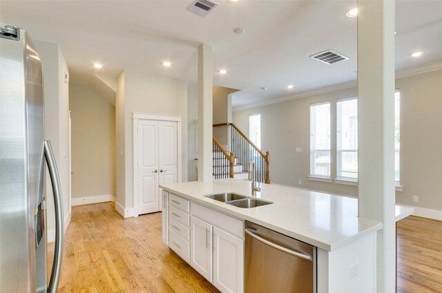 kitchen with white cabinets, sink, light wood-type flooring, an island with sink, and appliances with stainless steel finishes