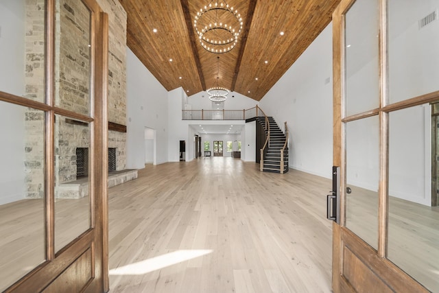 unfurnished living room featuring wooden ceiling, high vaulted ceiling, an inviting chandelier, a stone fireplace, and light hardwood / wood-style floors