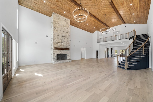 unfurnished living room with wooden ceiling, a stone fireplace, a towering ceiling, light wood-type flooring, and a notable chandelier