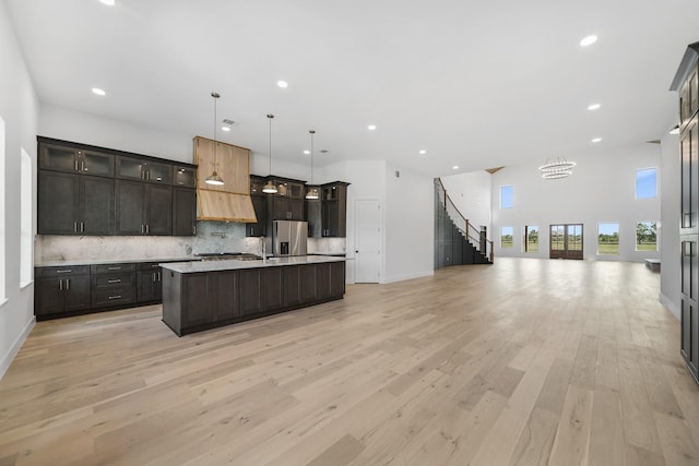 kitchen with stainless steel refrigerator with ice dispenser, dark brown cabinets, pendant lighting, a center island with sink, and light hardwood / wood-style flooring