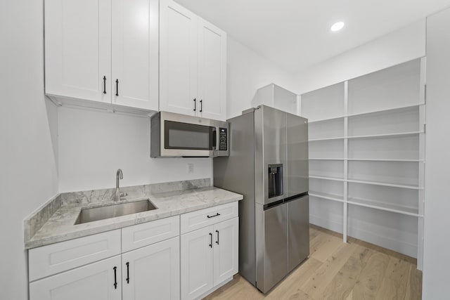 kitchen with white cabinets, stainless steel appliances, light stone counters, and sink