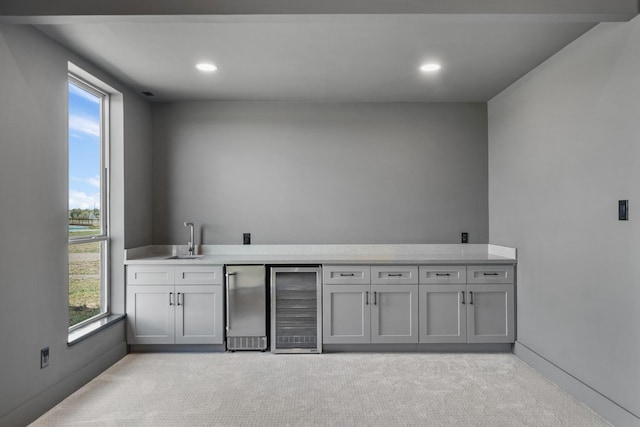 bar with sink, wine cooler, refrigerator, light colored carpet, and gray cabinets