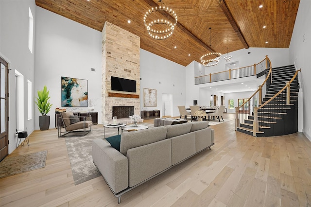 living room with light wood-type flooring, wooden ceiling, a chandelier, a high ceiling, and a stone fireplace