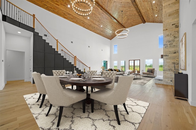 dining space featuring light wood-type flooring, a towering ceiling, an inviting chandelier, wooden ceiling, and beamed ceiling