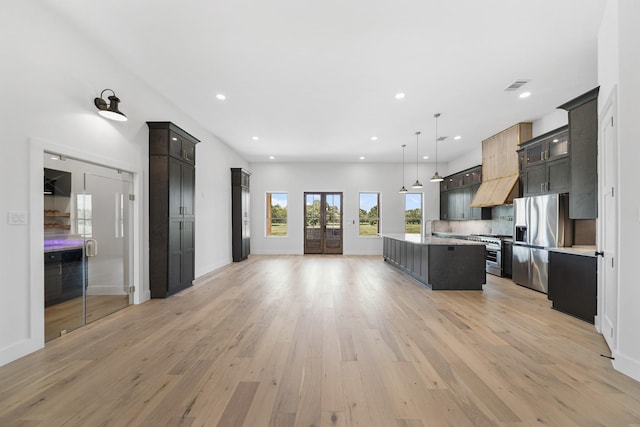 kitchen featuring decorative backsplash, light wood-type flooring, stainless steel appliances, decorative light fixtures, and a center island with sink