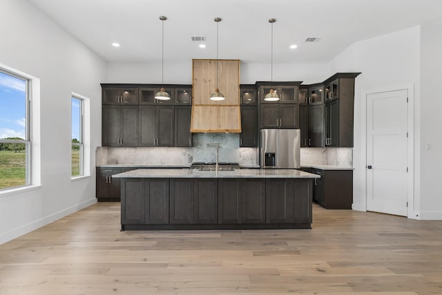 kitchen featuring light hardwood / wood-style flooring, stainless steel fridge with ice dispenser, an island with sink, decorative light fixtures, and dark brown cabinetry