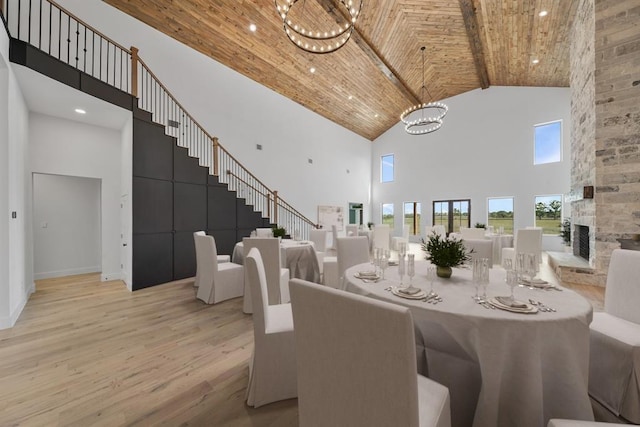 dining area with wooden ceiling, a stone fireplace, light hardwood / wood-style flooring, a towering ceiling, and beam ceiling