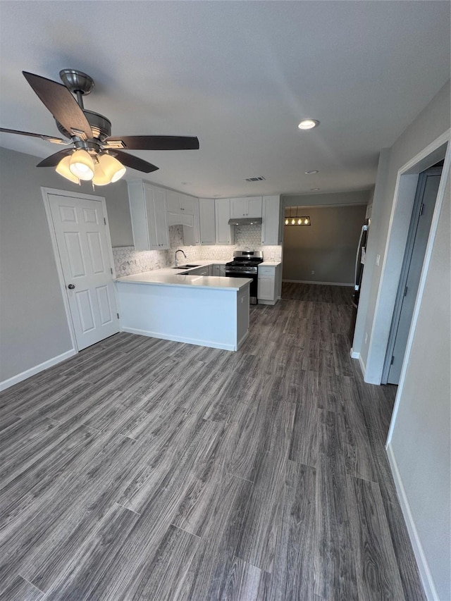 kitchen with sink, dark wood-type flooring, backsplash, stainless steel range oven, and kitchen peninsula