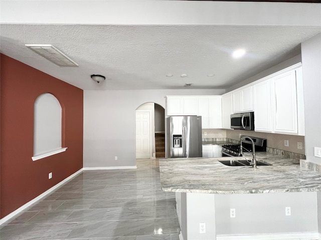 kitchen with white cabinets, light stone countertops, a textured ceiling, appliances with stainless steel finishes, and kitchen peninsula