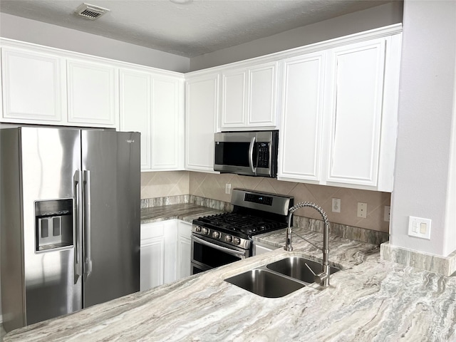 kitchen with decorative backsplash, light stone countertops, stainless steel appliances, sink, and white cabinets