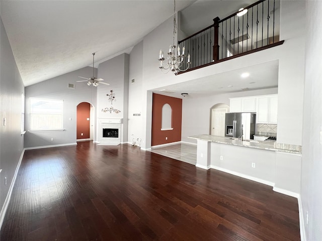 unfurnished living room with dark hardwood / wood-style floors, sink, ceiling fan with notable chandelier, and high vaulted ceiling