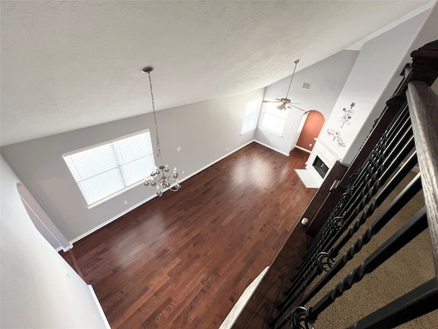 unfurnished living room with a textured ceiling, ceiling fan with notable chandelier, dark wood-type flooring, and high vaulted ceiling