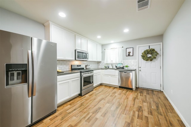 kitchen with white cabinets, appliances with stainless steel finishes, light wood-type flooring, and decorative backsplash