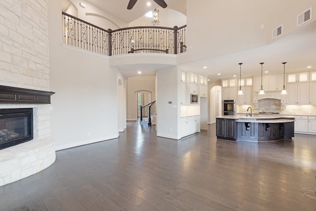 unfurnished living room with a large fireplace, ceiling fan, dark hardwood / wood-style flooring, and high vaulted ceiling