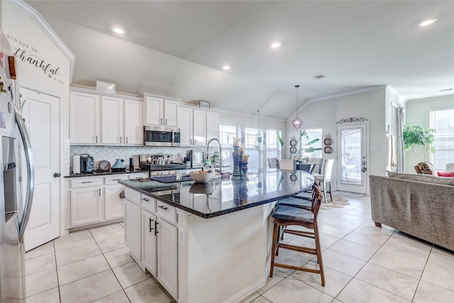 kitchen featuring white cabinets, stainless steel appliances, vaulted ceiling, and an island with sink