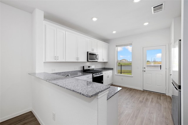 kitchen with kitchen peninsula, white cabinets, stainless steel appliances, and light wood-type flooring