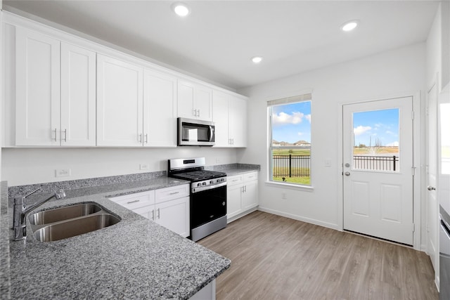 kitchen featuring white cabinets, sink, light hardwood / wood-style flooring, dark stone countertops, and appliances with stainless steel finishes