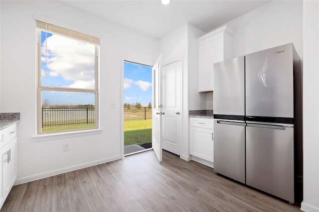 kitchen with white cabinets, light hardwood / wood-style floors, stainless steel refrigerator, and light stone counters