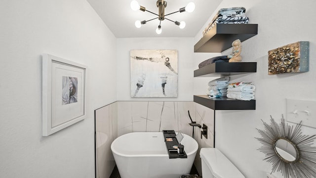 bathroom featuring a tub, toilet, tile walls, and a notable chandelier