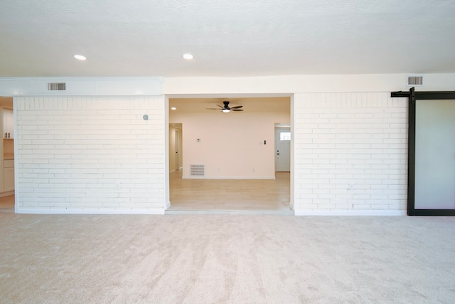 carpeted spare room with a barn door, ceiling fan, brick wall, and a textured ceiling