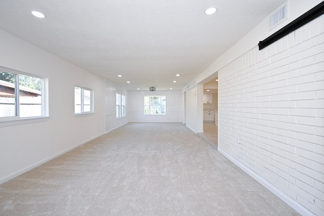 spare room with plenty of natural light, light colored carpet, and a textured ceiling