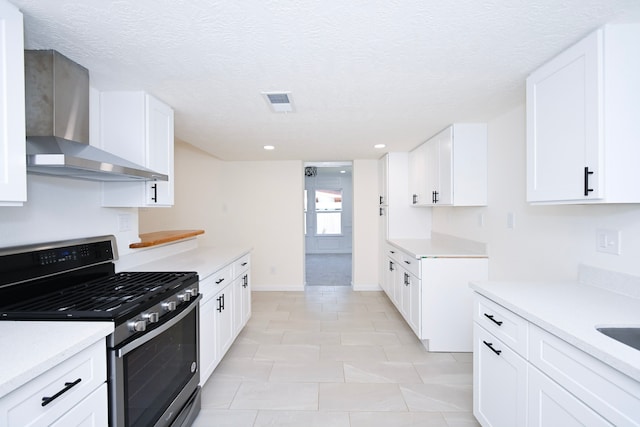 kitchen with wall chimney exhaust hood, a textured ceiling, light tile patterned floors, stainless steel gas stove, and white cabinetry