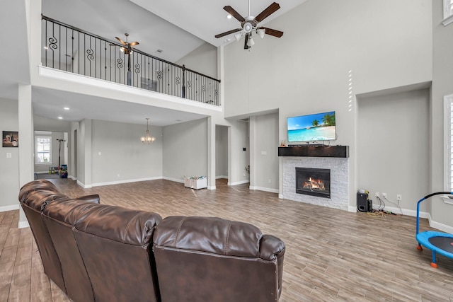 living room featuring wood-type flooring, ceiling fan with notable chandelier, high vaulted ceiling, and a stone fireplace