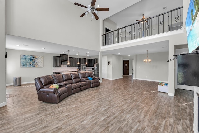 living room featuring hardwood / wood-style floors, ceiling fan with notable chandelier, and a towering ceiling