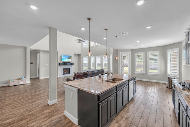 kitchen featuring a kitchen island with sink, sink, ceiling fan, light stone countertops, and appliances with stainless steel finishes