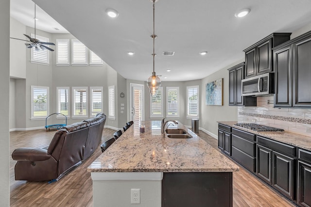 kitchen featuring sink, an island with sink, decorative light fixtures, decorative backsplash, and appliances with stainless steel finishes