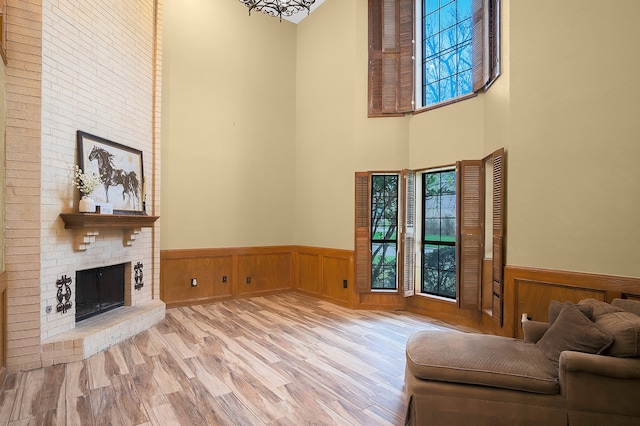 living room featuring a towering ceiling, light wood-type flooring, wooden walls, and a brick fireplace