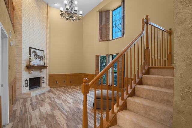 stairs featuring a towering ceiling, a brick fireplace, an inviting chandelier, hardwood / wood-style floors, and wood walls